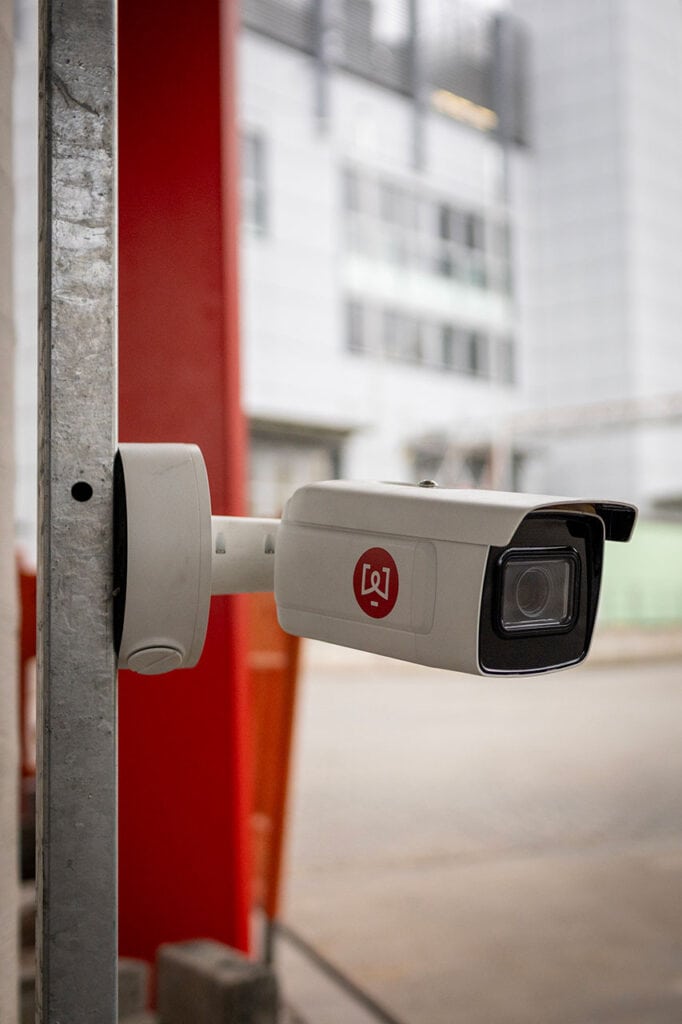 Camera voor nummerplaatherkenning gemonteerd naast rode zelfbedieningszuil voor voertuigweegschalen.